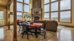 A spacious living room with a stone fireplace, large windows, and a view of the outdoors.