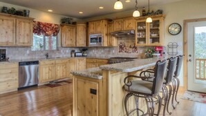 A kitchen with wooden cabinets, granite countertops, stainless steel appliances, and a bar area with bar stools.