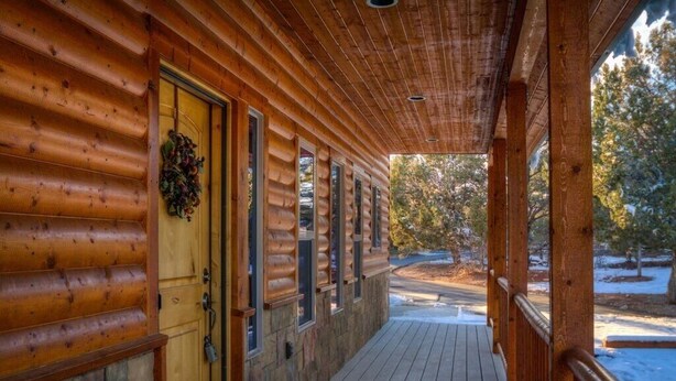 A wooden log cabin with a porch, stone foundation, and a door with a wreath.