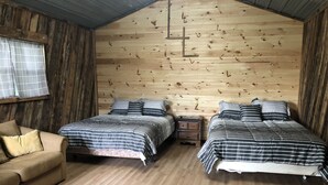 Et hyggeligt værelse i sommerhusstil med to senge, træloft og trægulv.
