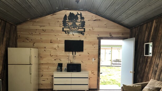 Et sommerhuse interiør med træloft, ophængt tv, køleskab, mikrobølgeovn og sofa.
