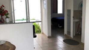 Habitación amplia con un ventanal, una mesa de madera, una cama y baño con lavamanos y estantes.