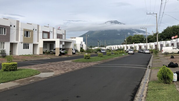 Una calle residencial con casas modernas, una vía despejada y una montaña al fondo.