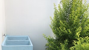 Pequeño espacio exterior amurallado con una caja de plantas azul, una planta en maceta y una rejilla metálica en el suelo.