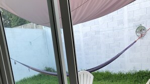 Puerta de vidrio que da a un patio con una silla blanca, una hamaca y una planta en maceta.
