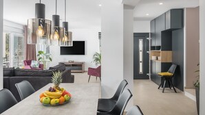 Una sala de estar moderna con comedor, televisor montado en la pared y frutero sobre la mesa.