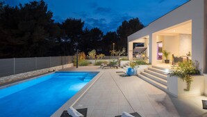 Un área de piscina moderna al aire libre con sillones de descanso y una zona de estar cubierta.