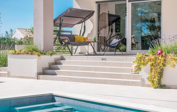 A poolside area with a chair and a table, a small outdoor kitchen, and steps leading to a glass door. - Luxurious home in Pula (Pula)