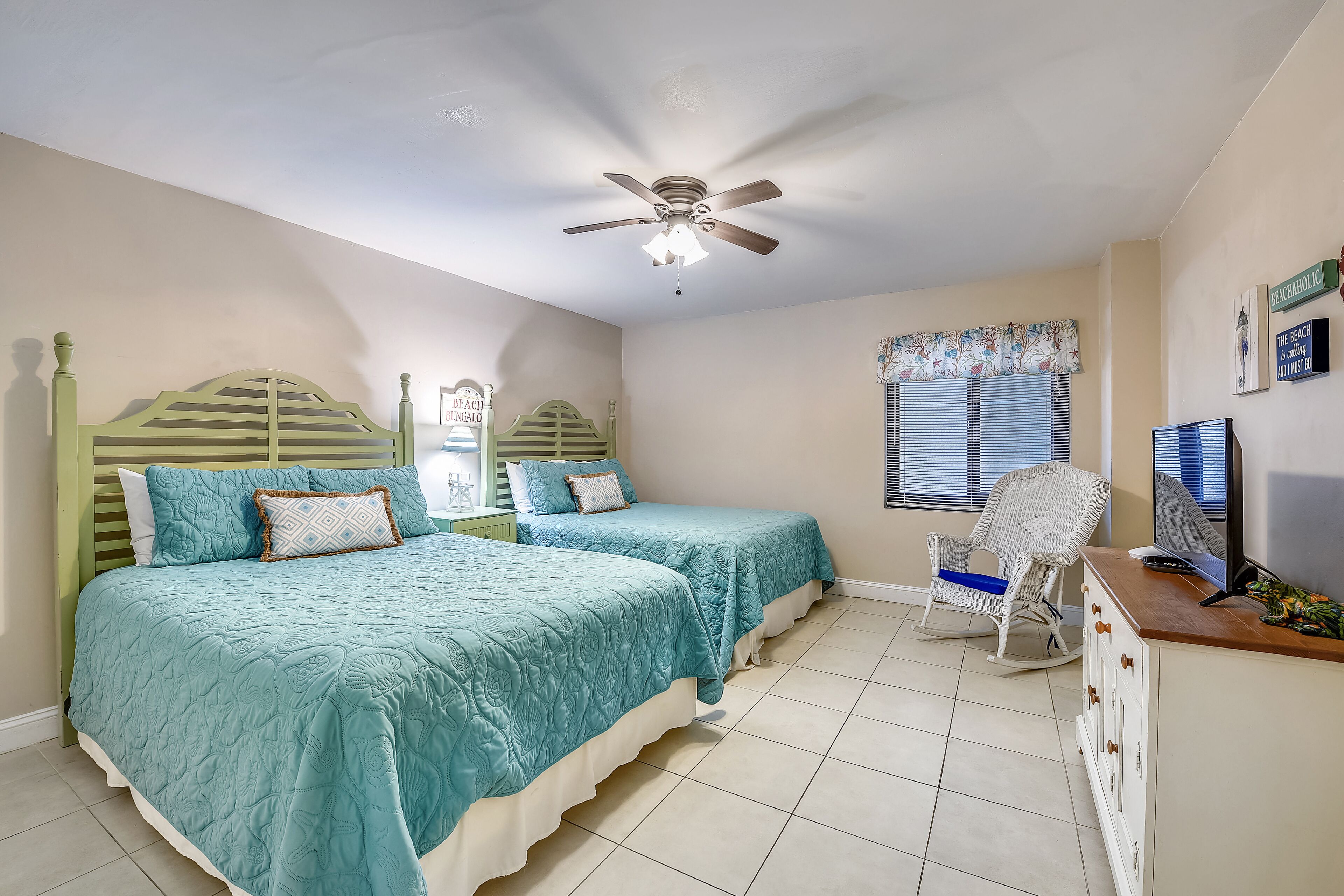 A bedroom with two beds, a ceiling fan, a rocking chair, a TV, and a window with blinds.