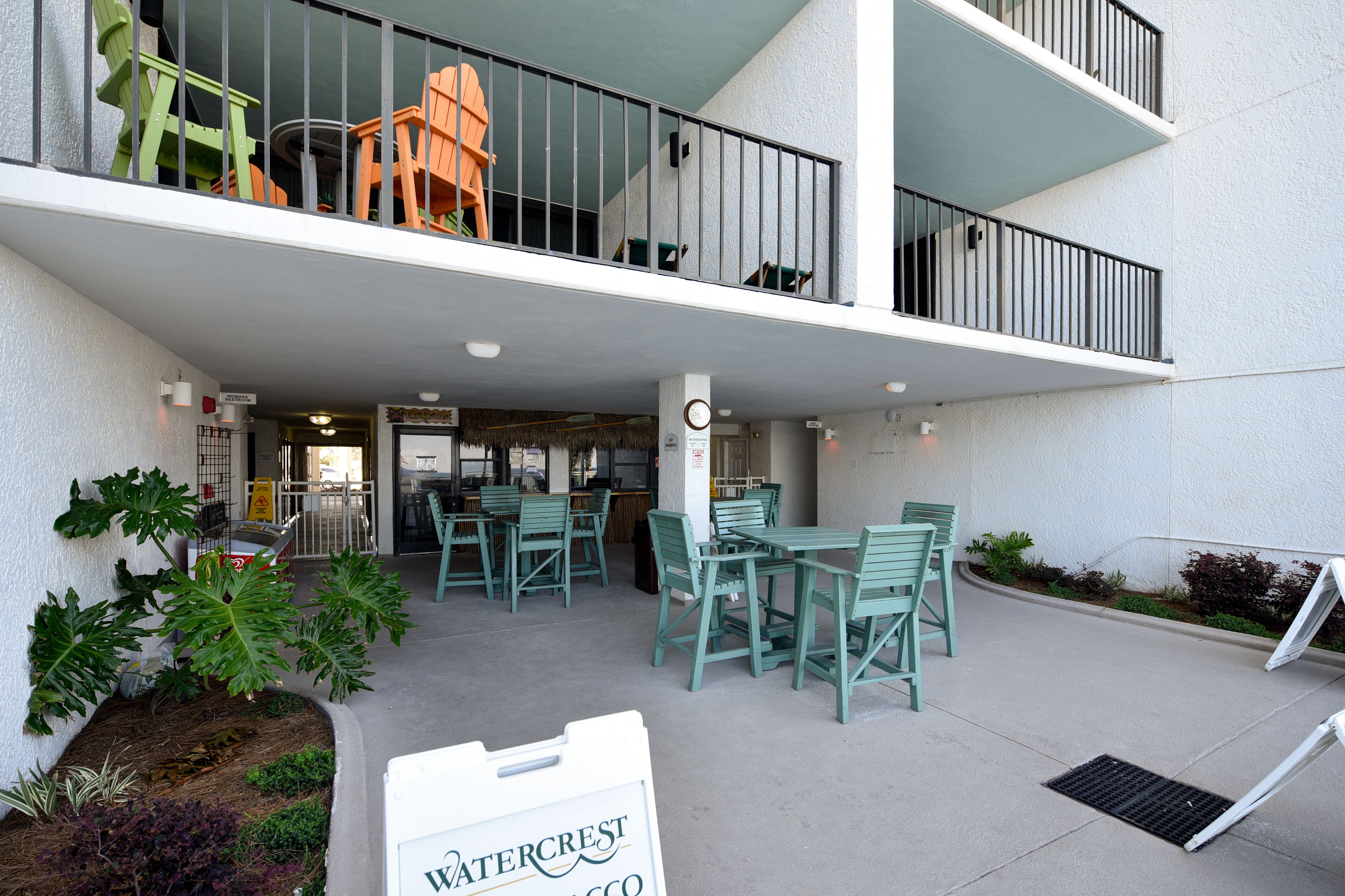 Een terras met groene stoelen en tafels, een bord met 'Watercrest' en een gebouw met een balkon.