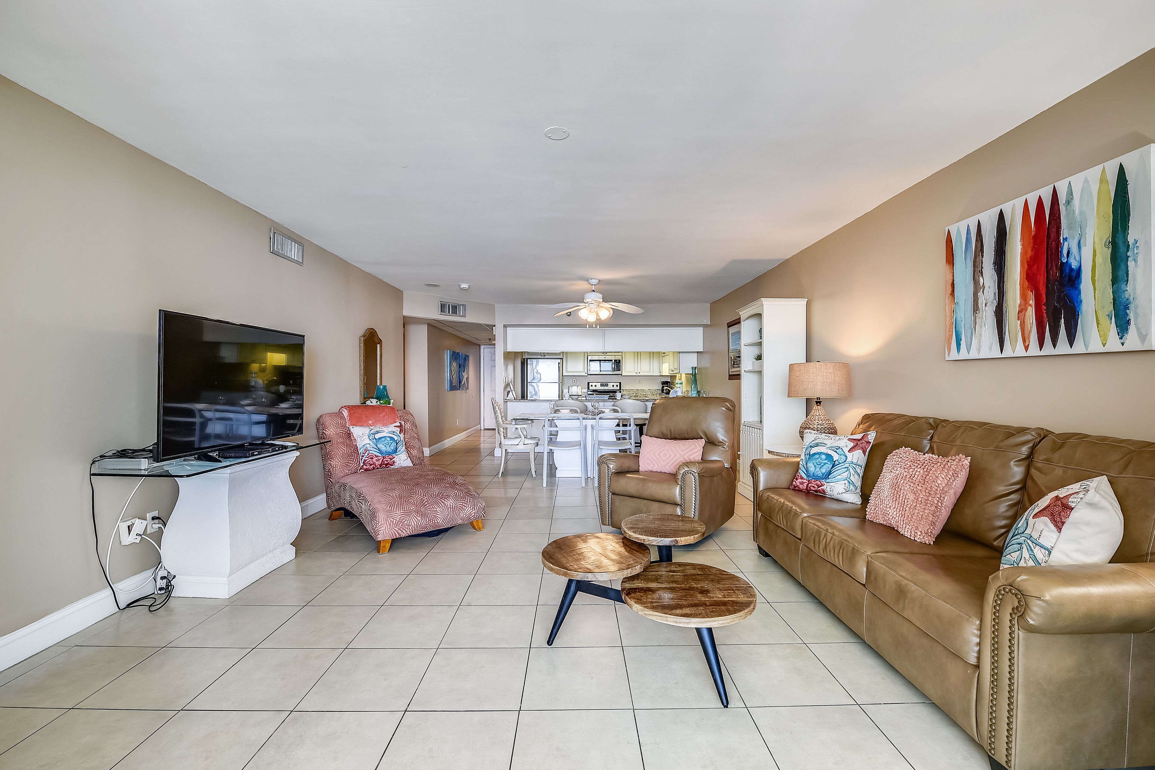 A spacious living room with a flat-screen TV, a brown leather sofa, a brown leather armchair, and a coffee table.