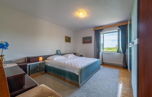 Quarto com cama, mesas de cabeceira, cômoda, janela com cortinas e vista para o exterior.
