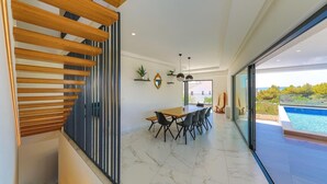 A modern dining area with a wooden table and chairs, a large mirror, and a view of a swimming pool.