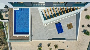 An aerial view of a modern building with a swimming pool, a covered outdoor area, and a staircase leading to a blue door.