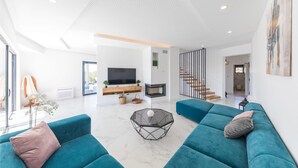 A spacious living room with teal sofas, a large TV, a fireplace, and a staircase leading to another level.