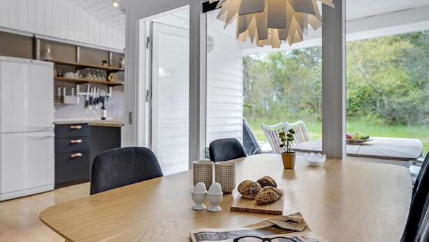 Une cuisine moderne avec des meubles blancs, une table à manger en bois et une vue sur l’extérieur.