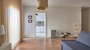 Una sala moderna con un sofá, una mesa de centro y un radiador. Se ve una cocina a través de una puerta abierta.