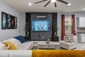 A modern living room with a flat-screen TV, a ceiling fan, and a kitchen area in the background. - Closest House to Resort • Star Wars Adventure + Home Theater! (Kissimmee)