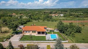 Ein Haus mit Schwimmbecken, umgeben von viel Grün und blauem Himmel.