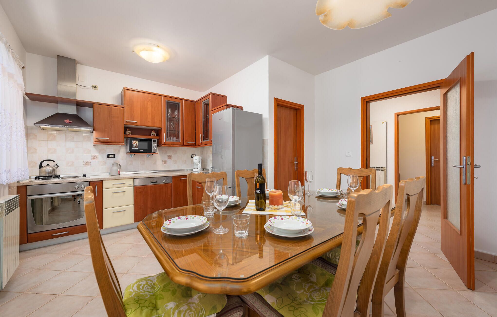 Une cuisine moderne avec des meubles en bois, une cuisinière en acier inoxydable et un coin repas doté d’une table en verre, mise pour quatre personnes.