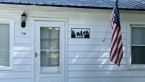 Uma casa branca com o número '110' na porta, uma bandeira americana e um letreiro com silhueta de animais.