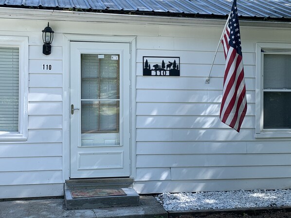 A white house with a number '110' on the door, an American flag, and a wildlife silhouette sign.