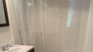 Casa de banho com sanita, lavatório, cortina de chuveiro e suporte para papel higiénico.