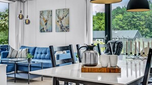 Een moderne woonkamer met een blauwe bank, een eettafel met een koffiepot en kopjes, en kunst aan de muur.