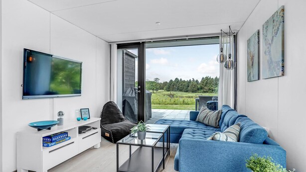 Een moderne woonkamer met een grote televisie, een bank, een salontafel en een glazen schuifdeur die uitkomt op een terras.