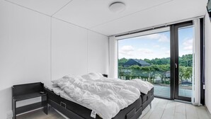 Een moderne slaapkamer met een groot bed, een nachtkastje en uitzicht op een meer en bomen.
