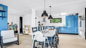 Een moderne keuken met een eethoek, met een witte tafel, blauwe kastjes en hanglampen.