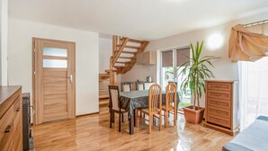 Un cuarto amplio con piso de madera, una mesa de comedor con sillas, una escalera, una zona de cocina y un gran ventanal con vistas.