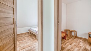 Una habitación con suelo de madera, una cama con colcha estampada, dos taburetes de madera y una pequeña mesa de madera.