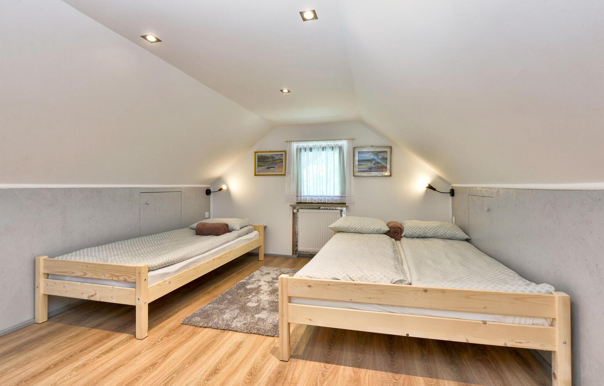A small, well-lit attic bedroom with two wooden bunk beds, a window with sheer curtains, and a radiator.