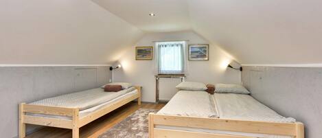 A small, well-lit attic bedroom with two wooden bunk beds, a window with sheer curtains, and a radiator.