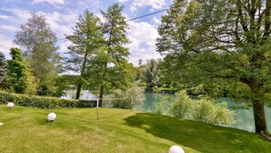 A serene outdoor area with a netted badminton court, surrounded by lush greenery and a calm lake.