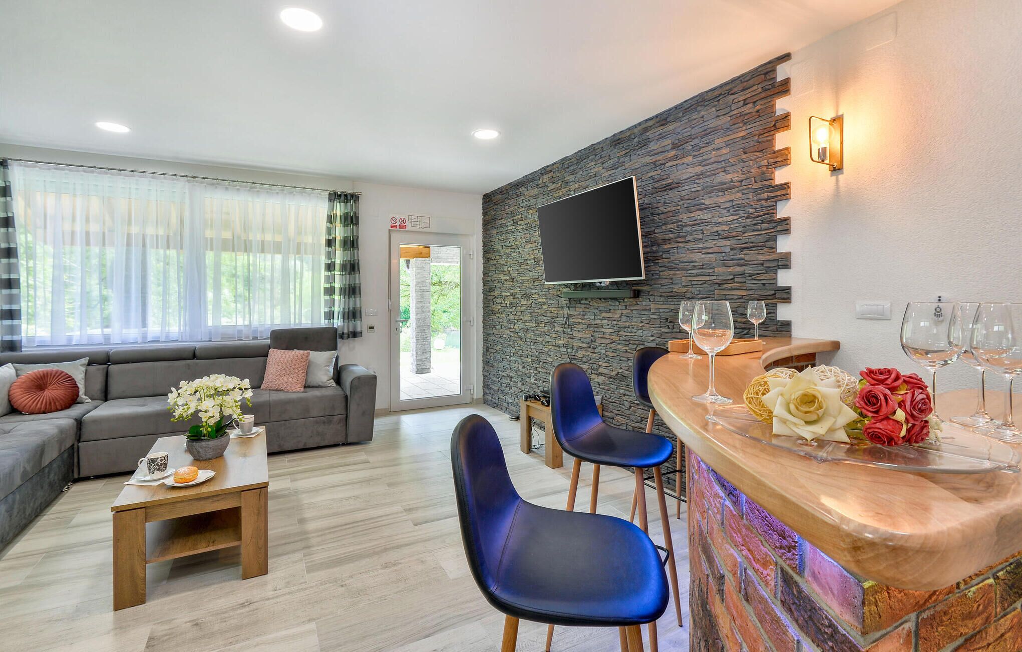 A modern living room with a grey sofa, blue chairs, a wooden coffee table, and a stone wall with a mounted TV.