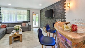 A modern living room with a grey sofa, blue chairs, a wooden coffee table, and a stone wall with a mounted TV.