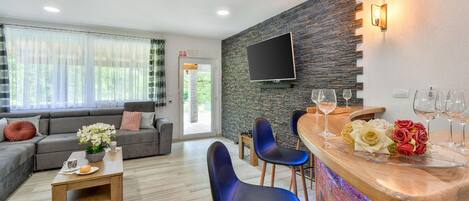 A modern living room with a grey sofa, blue chairs, a wooden coffee table, and a stone wall with a mounted TV.