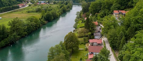 A riverside village with houses along the riverbank, a bridge in the distance, and a hilly landscape.