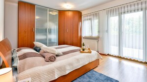 A bedroom with a large bed, wooden wardrobe, and a window with sheer curtains.