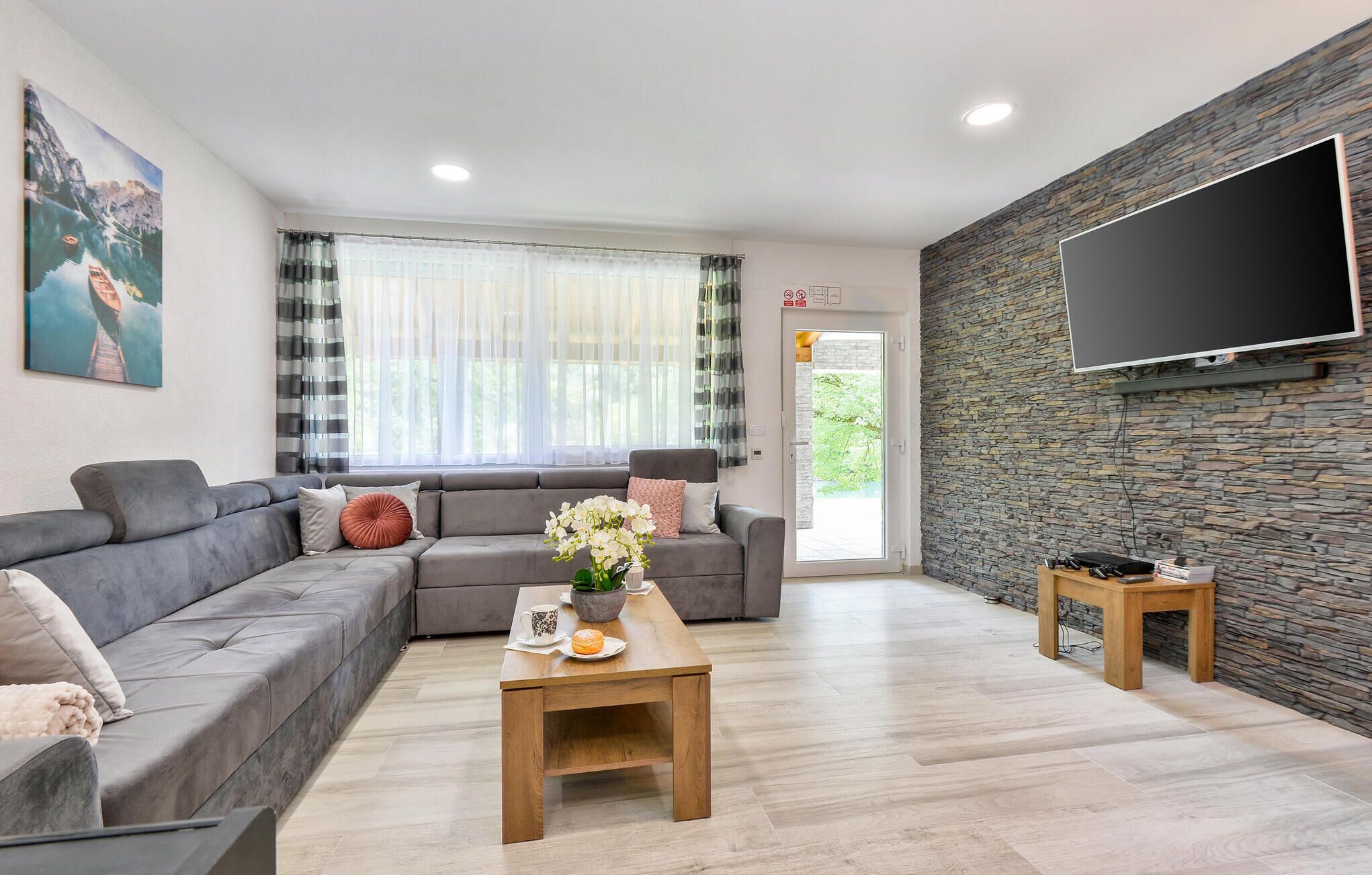 A modern living room with a grey sofa, a wooden coffee table, and a stone wall with a mounted TV.