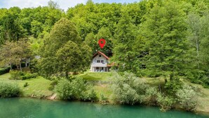 A house with a red roof, surrounded by lush greenery and a river.