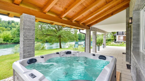 A hot tub under a wooden pergola with a river view.