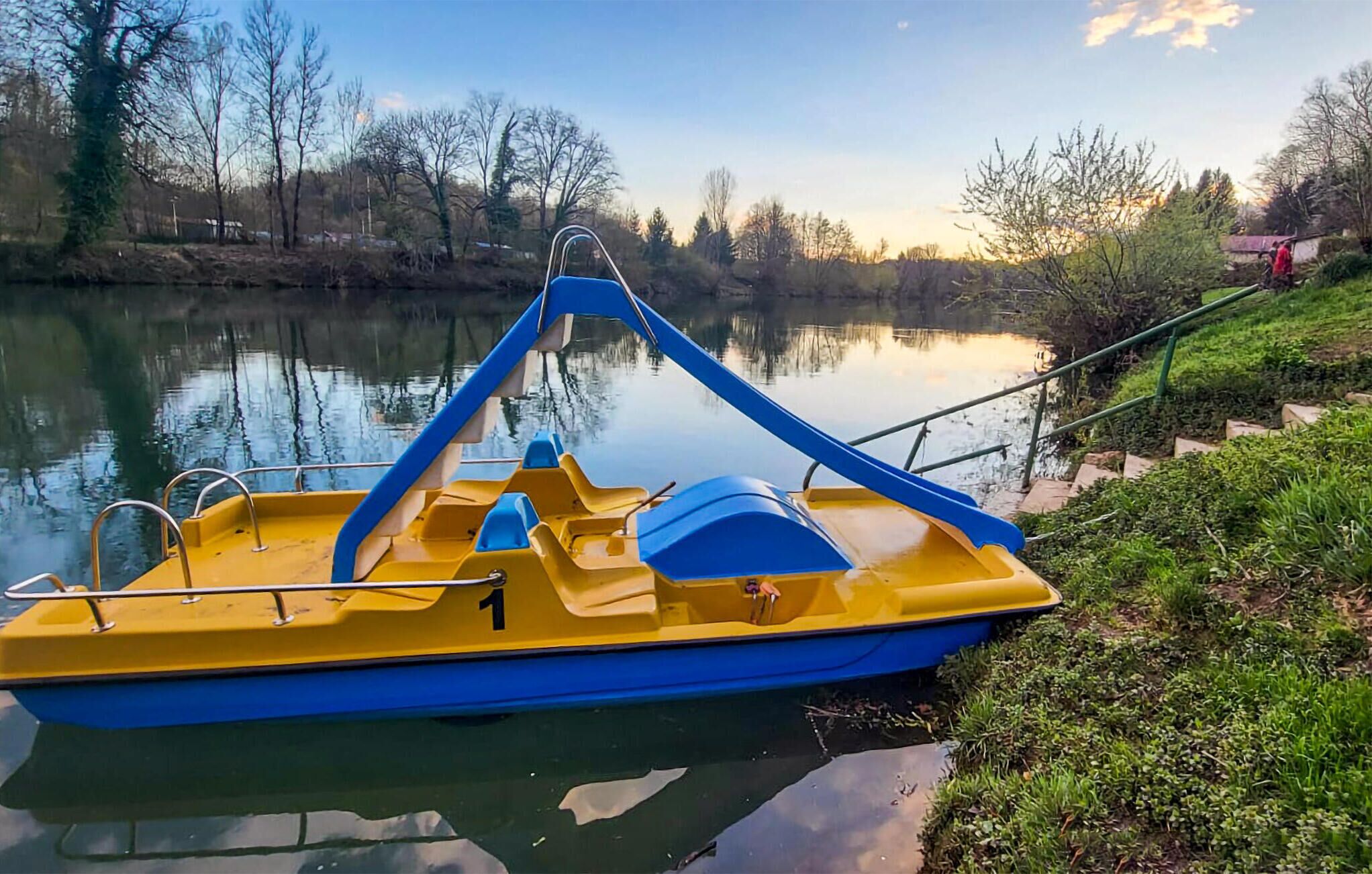 Un bateau jaune et bleu était amarré sur une rivière paisible, bordée d’une rive herbeuse et avec des arbres en arrière-plan.