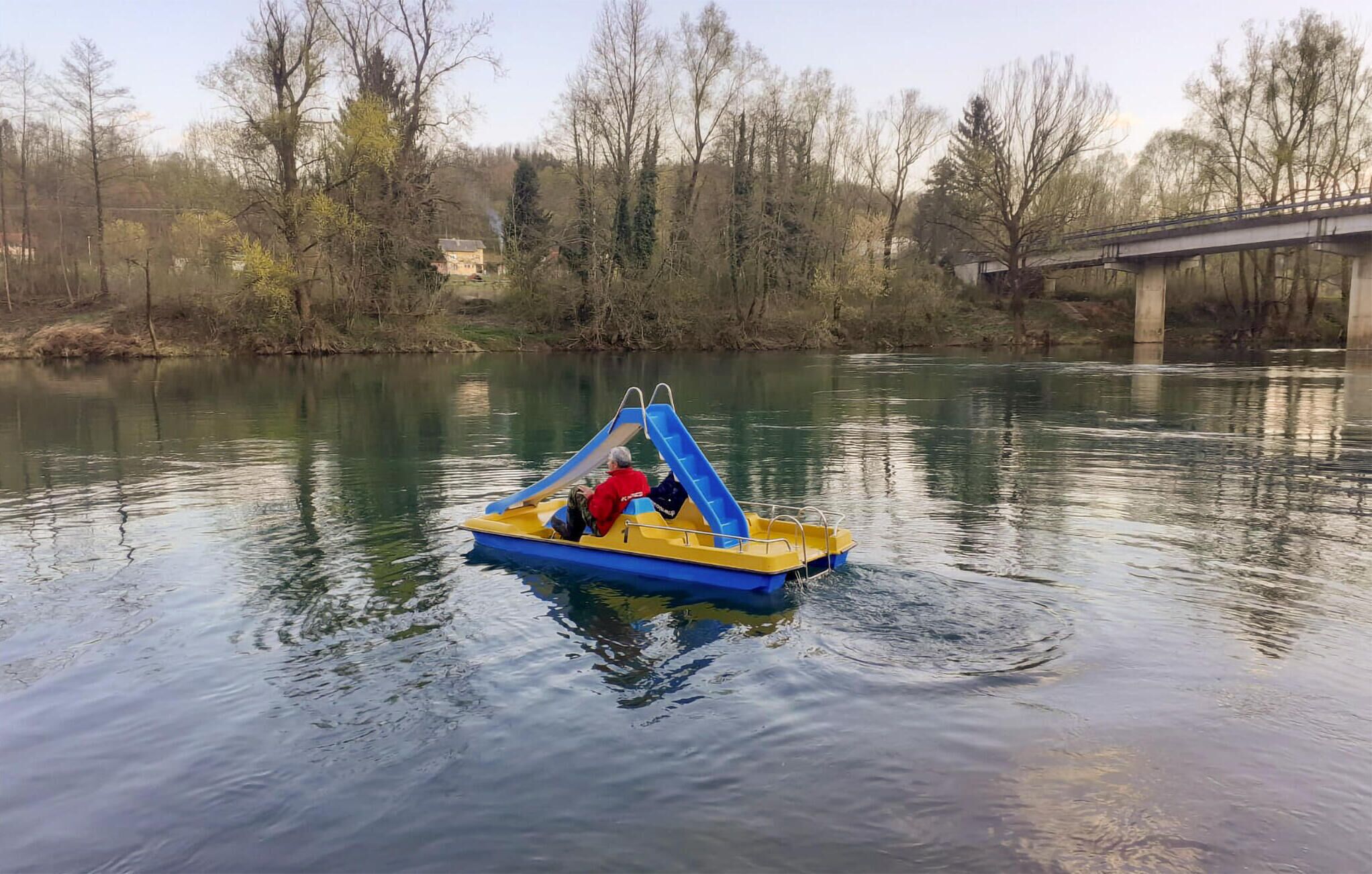 A small, yellow and blue boat with a slide on a calm river.