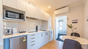 A compact kitchen with a microwave, toaster, and small refrigerator. There is a dining area with a table and chairs, and a view of the outside through a door. - Matariki Star - 1 Bedroom Suite A (Lake Tekapo)