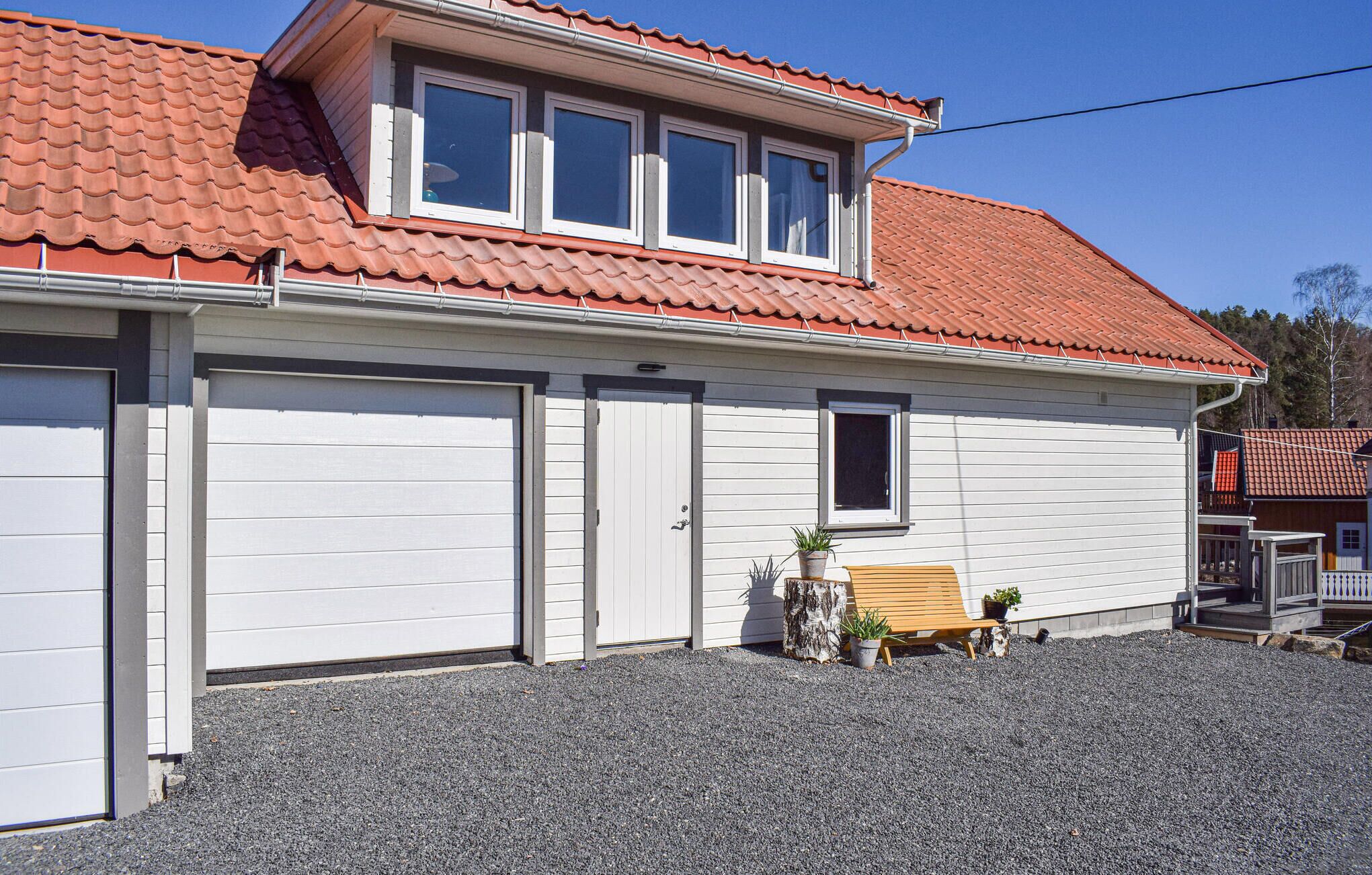 A single-story house with a red-tiled roof, two garage doors, and a small porch with a bench and potted plants.