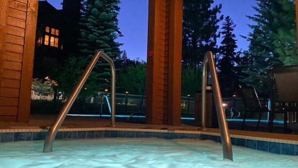 Un jacuzzi con escalones metálicos, rodeado por una terraza de madera y árboles.