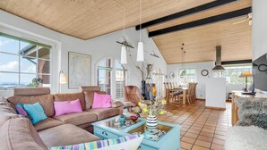 Een ruime woonkamer met een hoge nok, een eethoek en grote ramen met uitzicht.